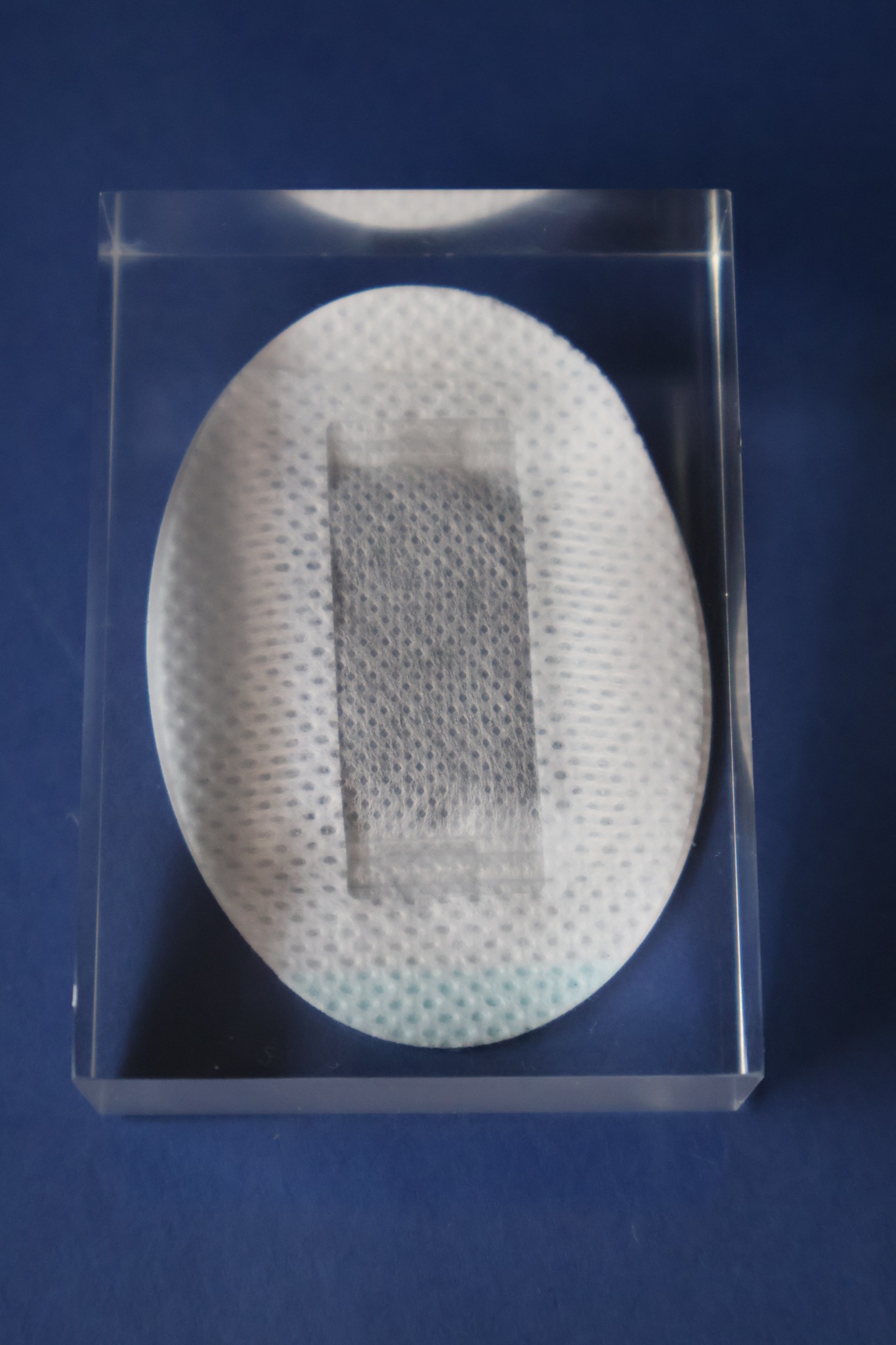 A single compact white patch displayed on a transparent acrylic block against navy.